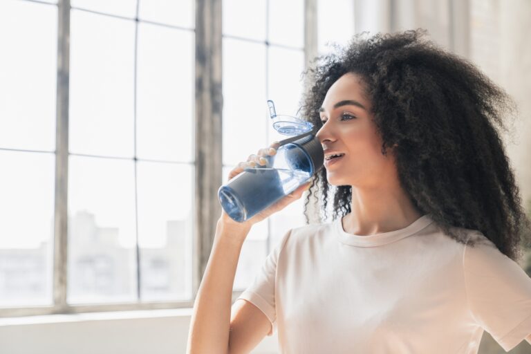 Happy black woman with water bottle for hydration in health and wellness at home.